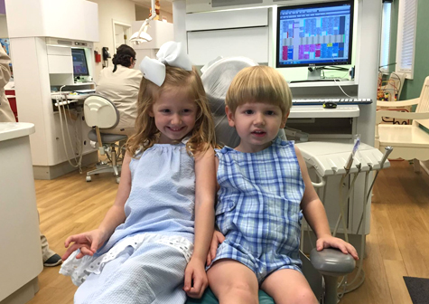 Two young children sitting in a dental examination chair in a pediatric dental office.