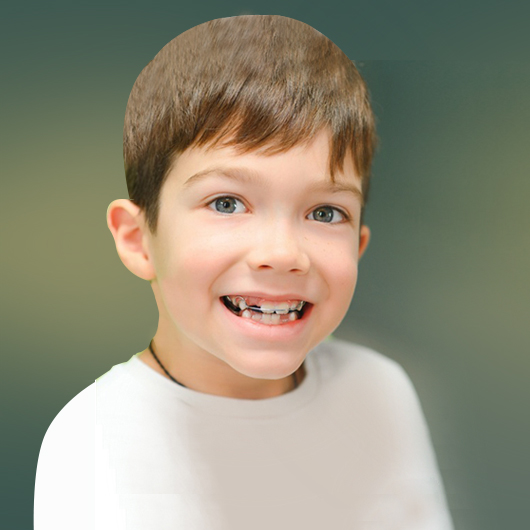 Young boy smiling at camera wearing white shirt against green background, pediatric dental portrait.