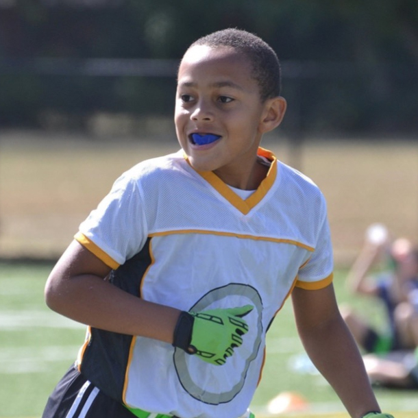 Young child wearing sports jersey with blue lipstick on outdoor athletic field.