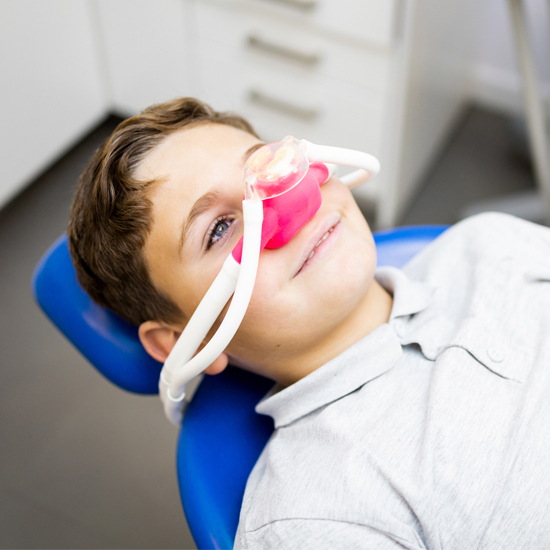 Child receiving dental treatment in office, wearing protective nasal mask and blue headrest.