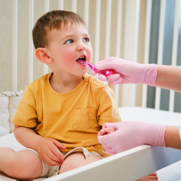 Young child in yellow shirt receiving dental examination from dentist wearing pink gloves in clinical setting.